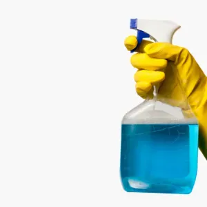 A gloved hand holds a spray bottle filled with blue liquid against a white background.
