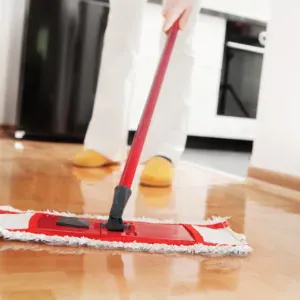 A person is mopping a shiny wooden floor with a red mop.